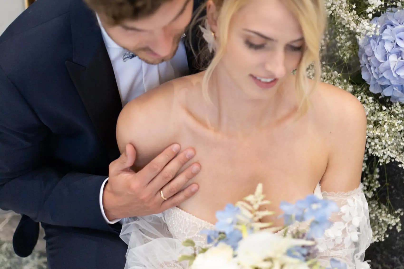 Lo sposo appoggia la mano sulla spalla della sposa fra le ortensie azzurre