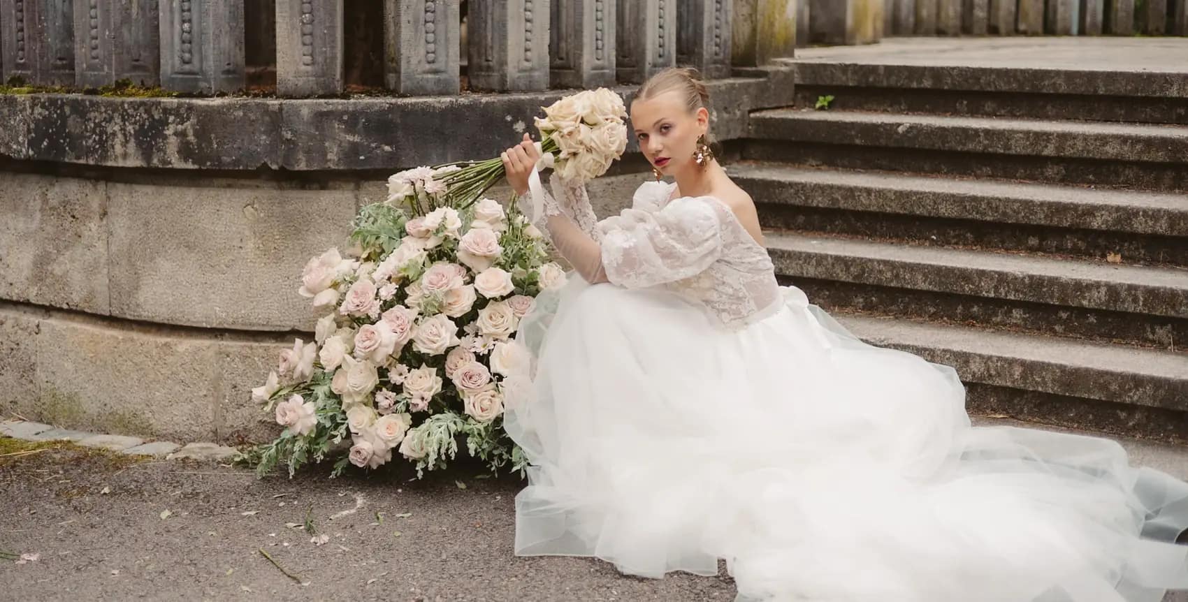Sposa seduta sulla scalinata di una villa accanto a una cascata di rose chiare